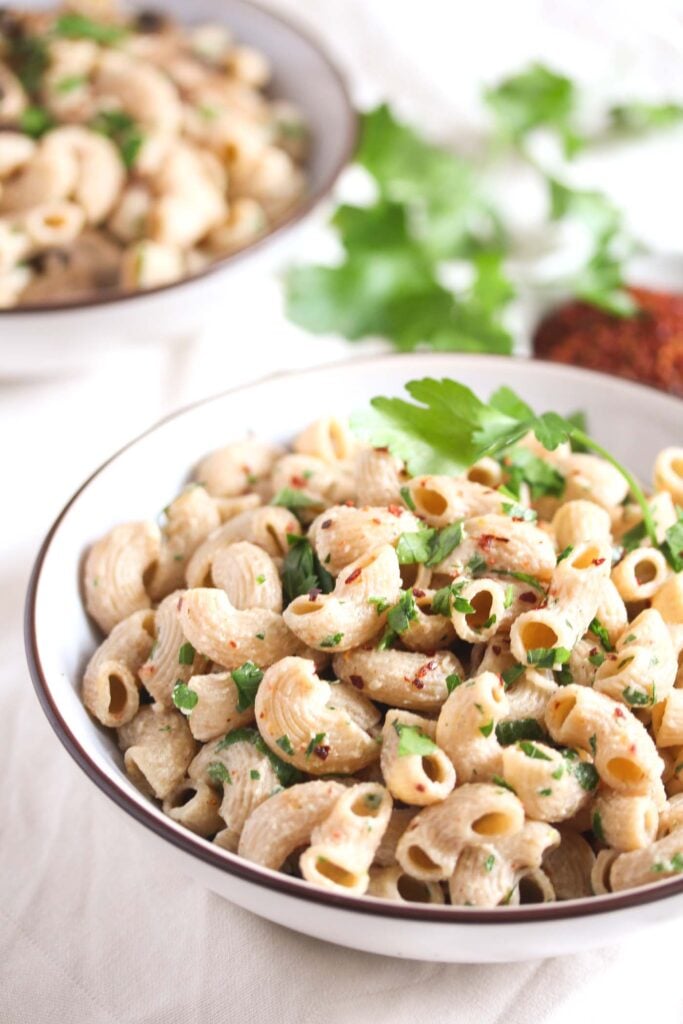 two bowls of whole wheat macaraoni sprinkled with parsley.