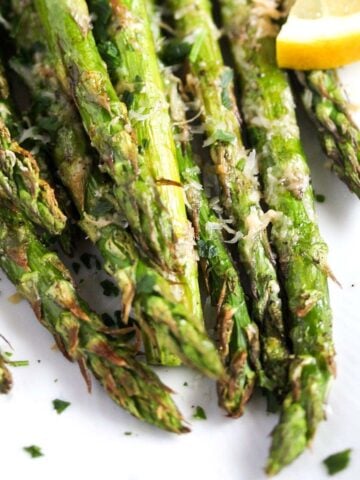 close up of air fryer asparagus sprinkled with parmesan on a white plate.