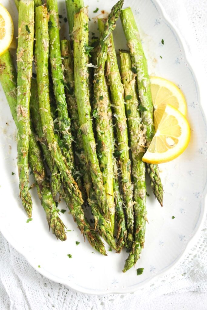 air fried asparagus with lemon wedges on a large long shaped platter.