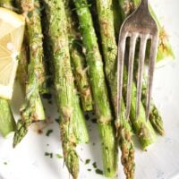 asparagus cooked in the air fryer on a white platter with a vintage fork on the side.