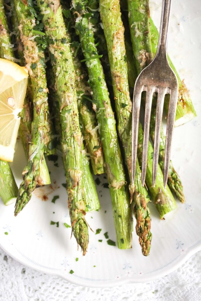 asparagus cooked in the air fryer on a white platter with a vintage fork on the side.