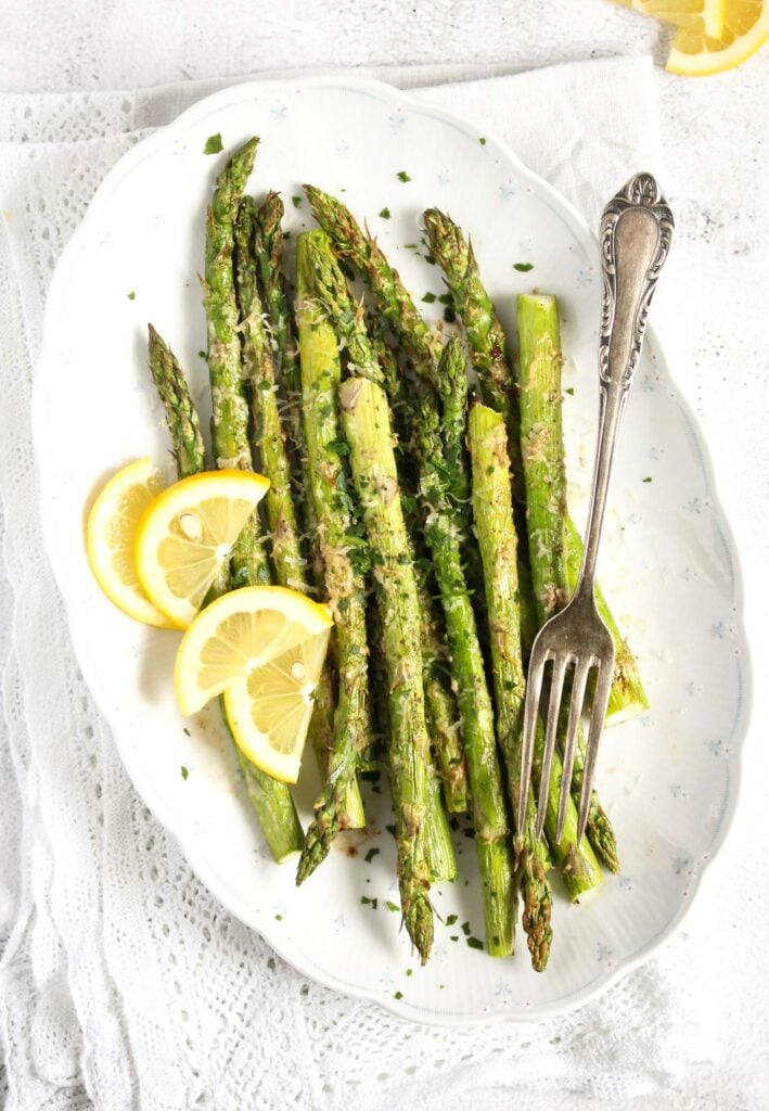 platter of roasted asparagus spears served with lemon wedges on the table.