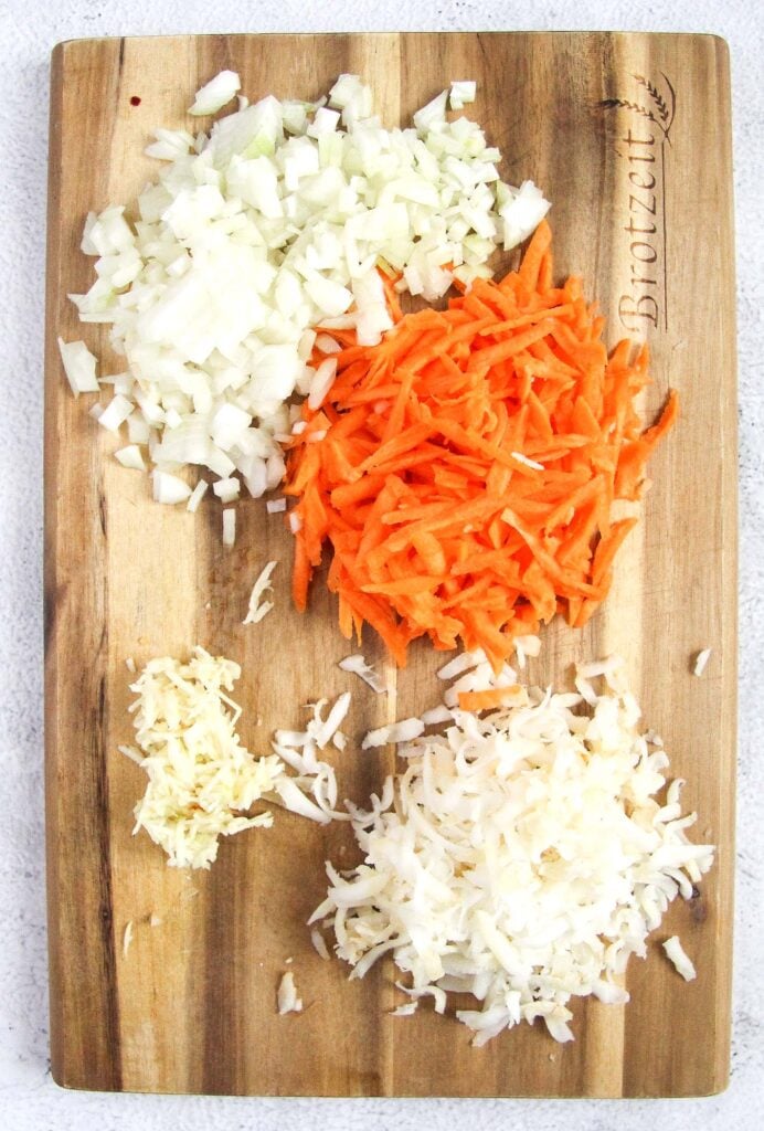 chopped onion, grated carrots, garlic and celeriac on a wooden board.