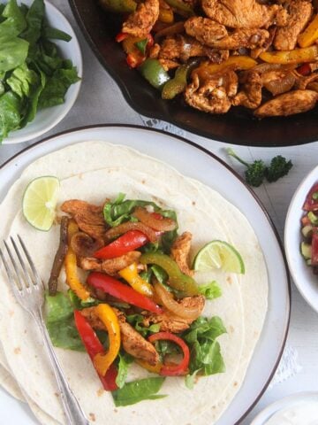 chicken fajita tacos on a plate and a skillet and bowls with toppings around it.