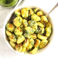 overhead shot of pesto gnocchi in a small bowl with a fork sticking in them.