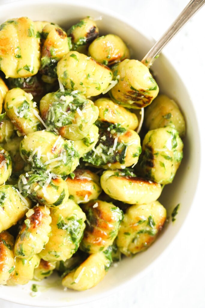 gnocchi with pesto and cream in a small white bowl.