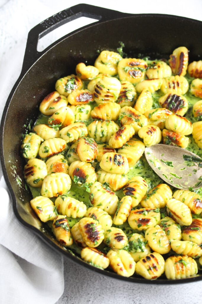 potato dumplings with creamy green sauce in a cast iron pan with a spoon in it.