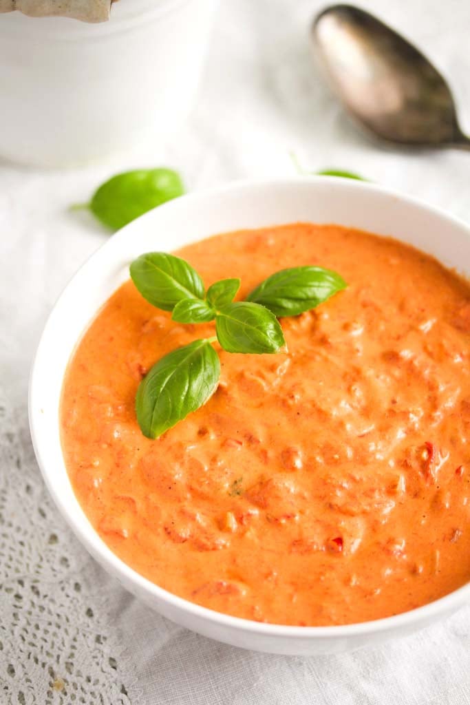 bowl of creamy tomato and cream cheese sauce with basil leaves on top.