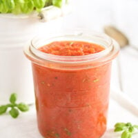 napoli tomato sauce for pizza in a small jar, a basil plant behind it.