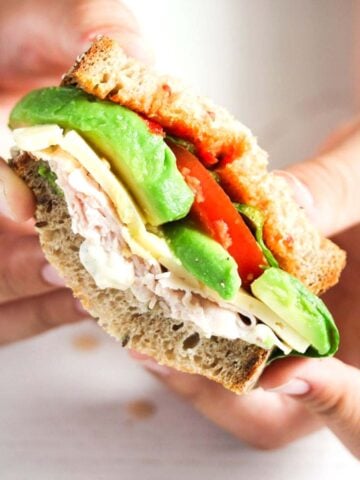 boy's hands holding a halved turkey avocado sandwich.