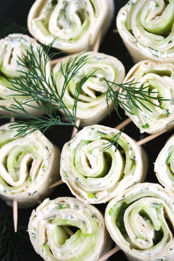 many small pinwheels with cucumber and cream cheese decorated with fresh dill.
