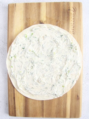 spreading cream cheese and dill mixtures on a tortilla.