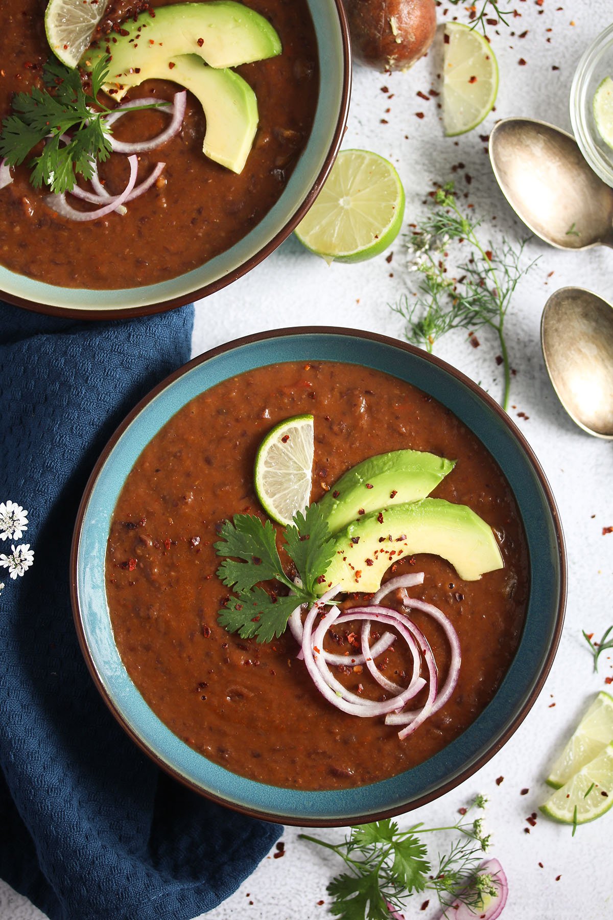 panera black bean soup garnished with avocado, onion and cilantro in bowls. 