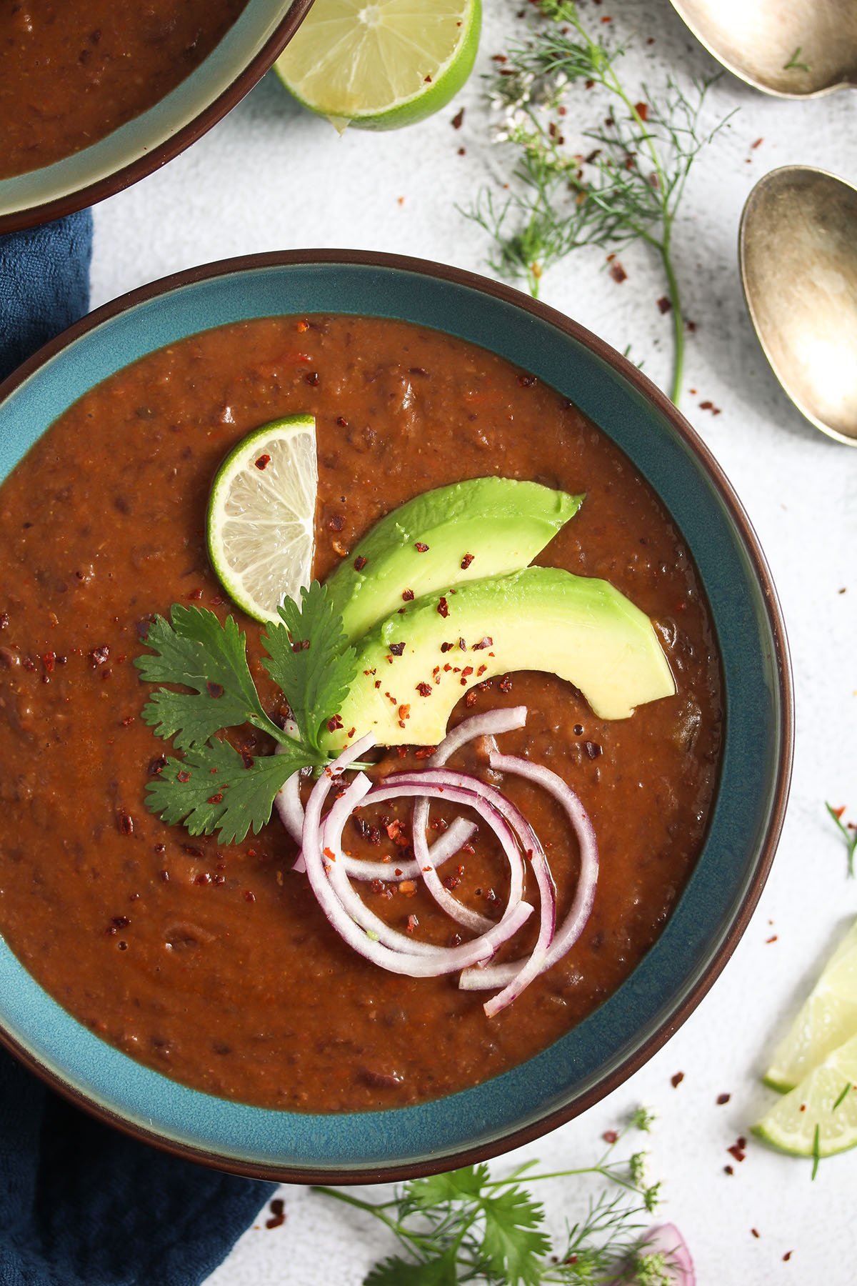 black bean soup panera restaurant style in a blue bowl with onions and avocado.