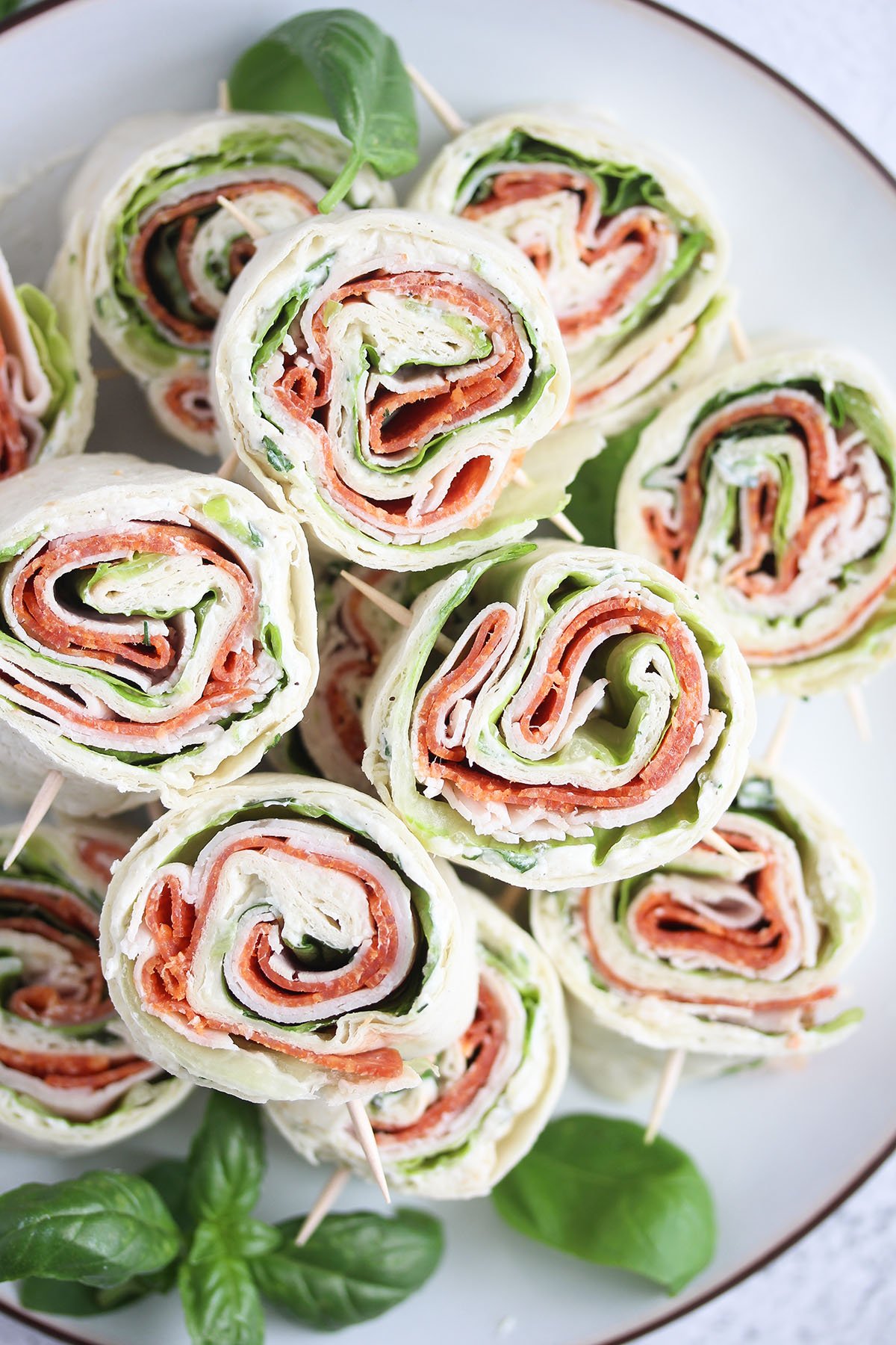 many pinwheel sandwiches stapled on a plate with basil.
