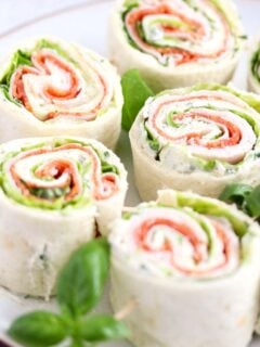 sandwich pinwheels arranged on a plate with basil leaves between them.