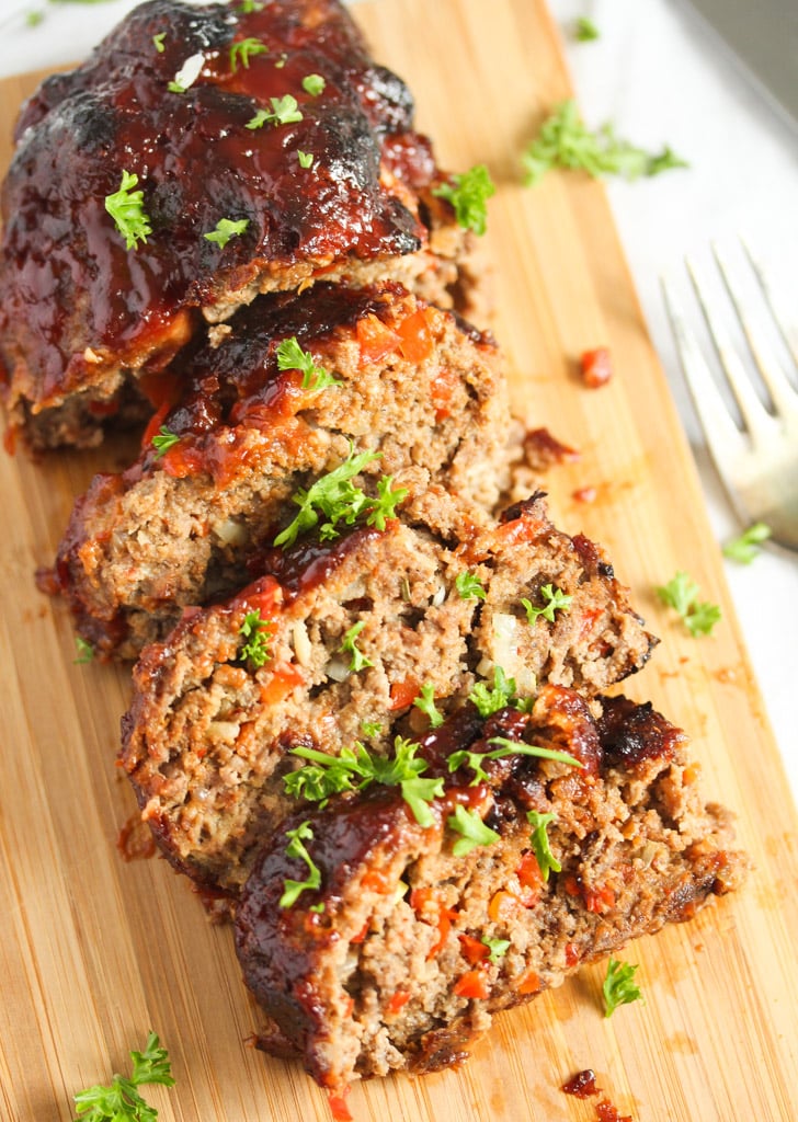 sliced meat loaf spiked with red bell peppers on a cutting board.