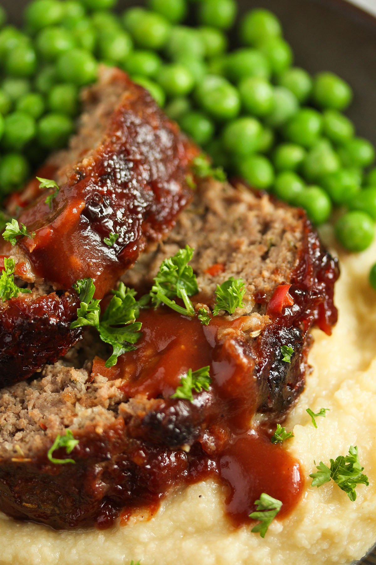 sliced air fryer meatloaf drizzled with gravy and served with mash and green peas. 