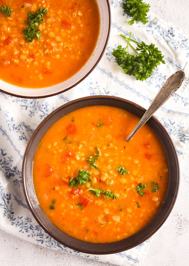 two bowls of orange colored food with lentils and tomatoes.