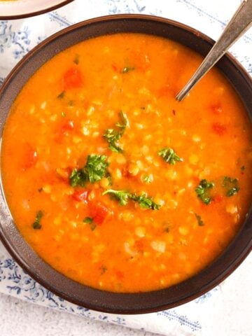 lebanese lentil soup with tomatoes and parsley in a brown bowl.