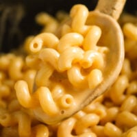 wooden spoon lifting super creamy mac and cheese from a pot.