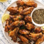 close up of many wings on a plate with a bowl of spices.