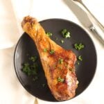 overhead pictures of a large turkey drumstick on a black plate with fork behind.