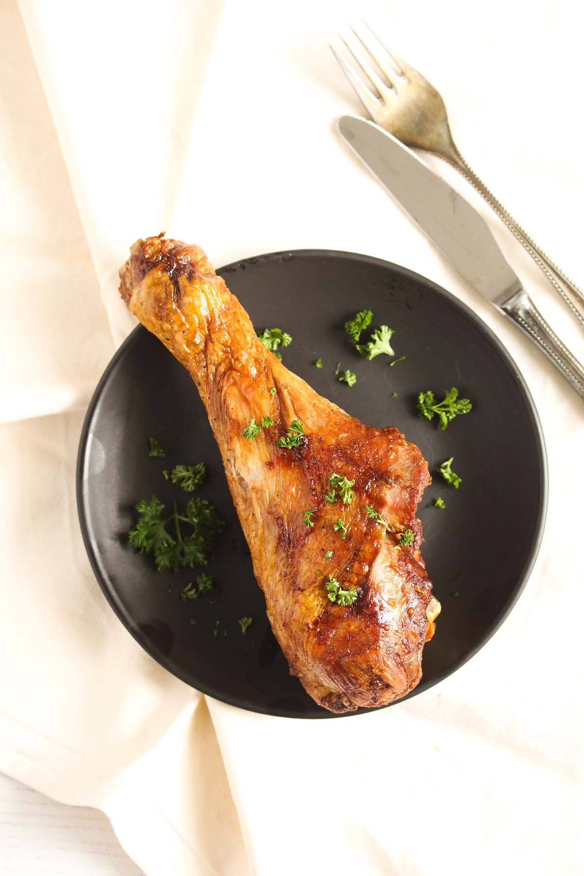 overhead pictures of a large turkey drumstick on a black plate with fork behind.