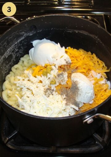 macaroni in a pot with dollops of cheese and cream cheese on top before stirring.