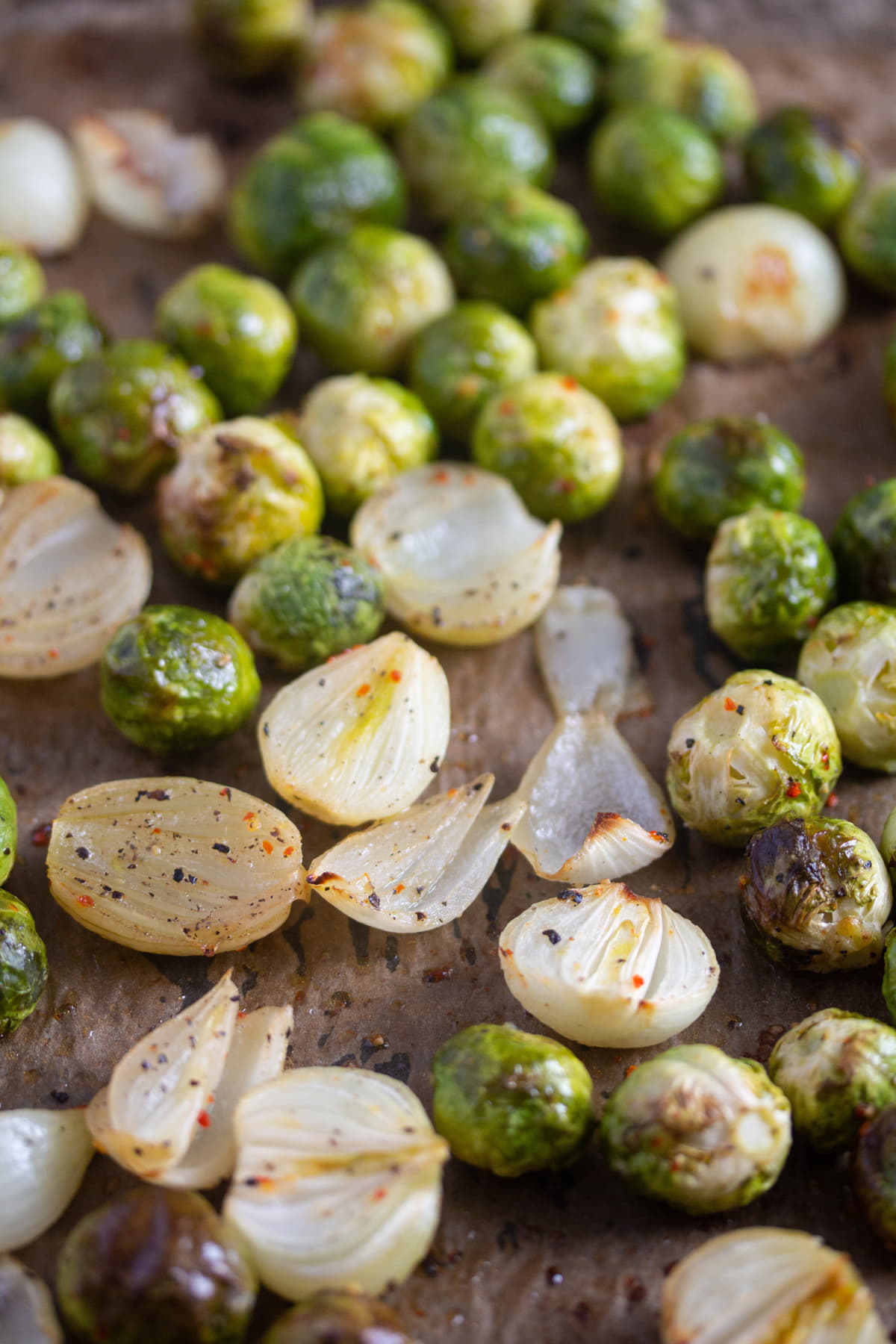 many halved shallots and small brussels sprouts with hot sauce on a tray.