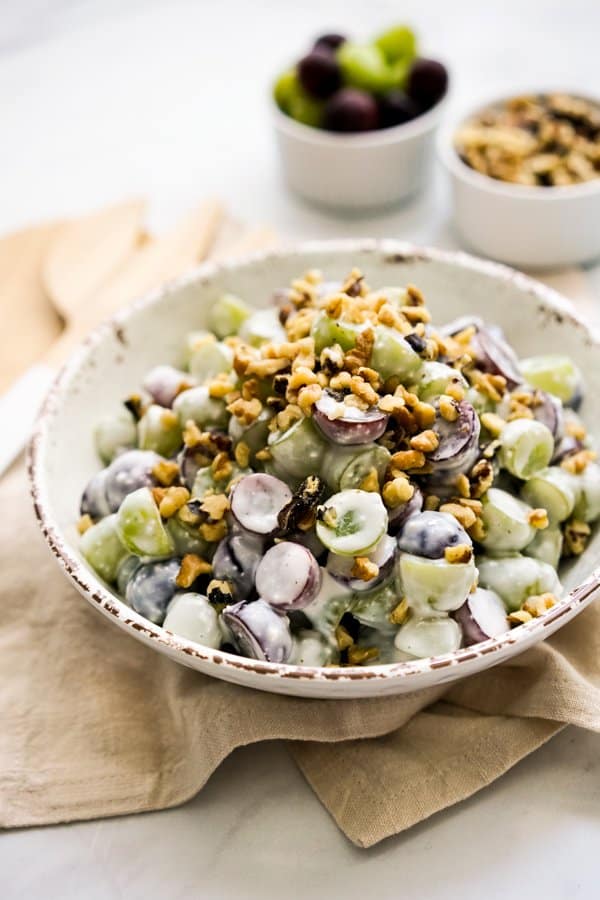 bowl of creamy salad with grapes and walnuts, two small bowls with toppings behind it.
