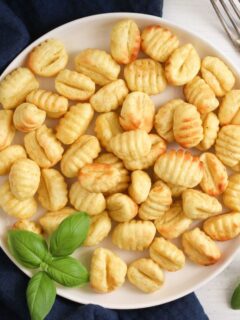 golden air fryer gnocchi with basil on a white plate.