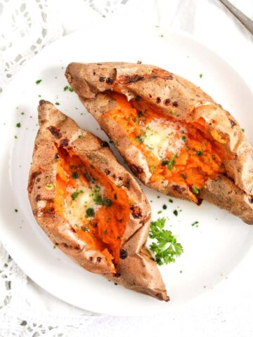 air fryer baked sweet potatoes served with butter and parsley on a plate.