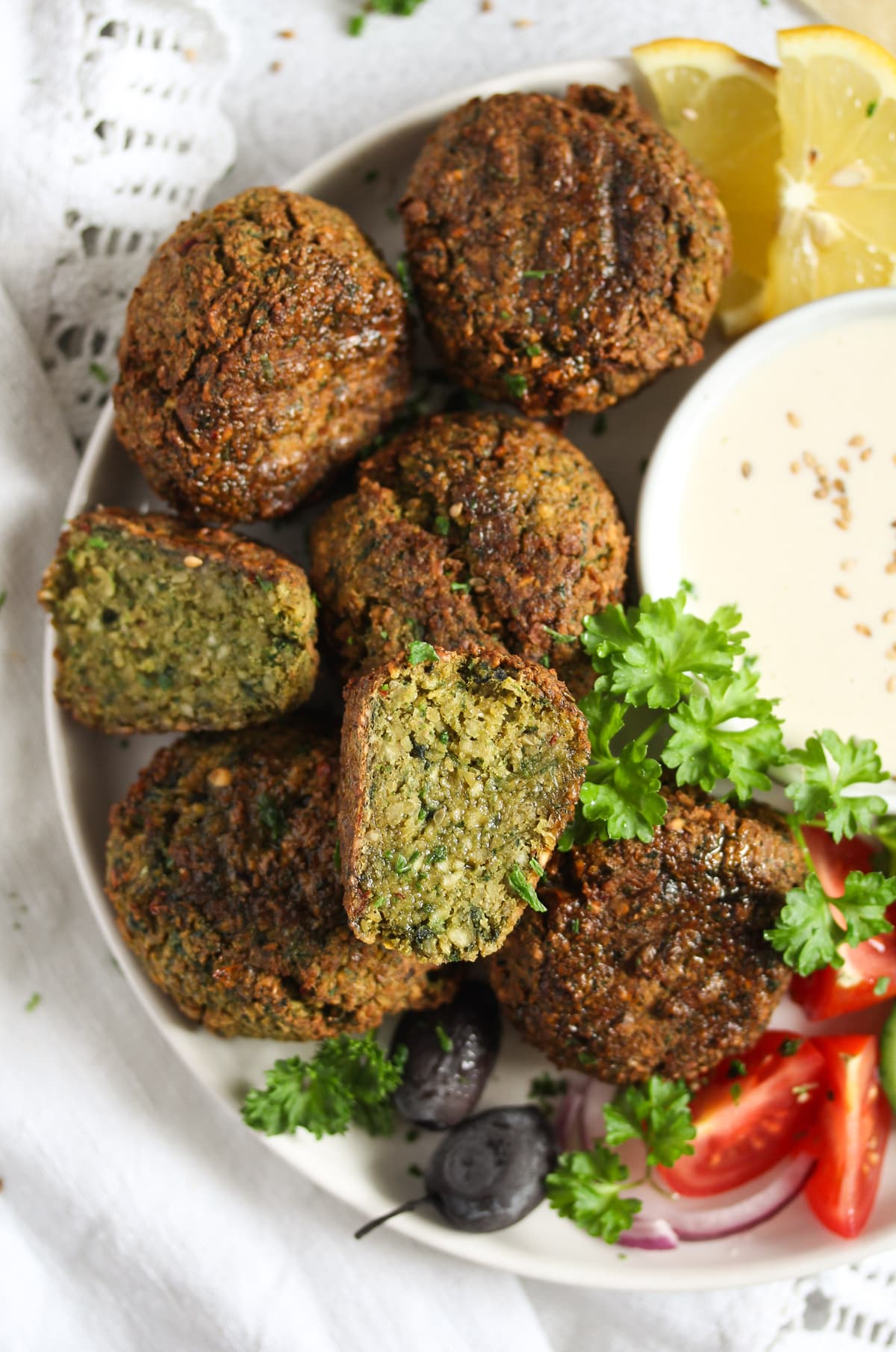 many crisp falafel with tahini sauce on a plate.