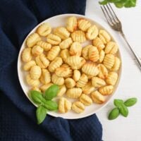 overhead view of a small plate with potato dumplings on a dark cloth with basil.