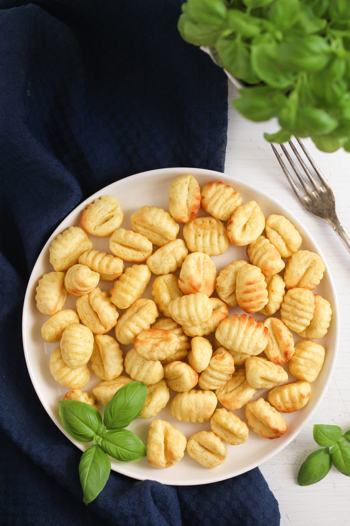 plate with gnocchi fried in the air fryer and a bunch of basil.