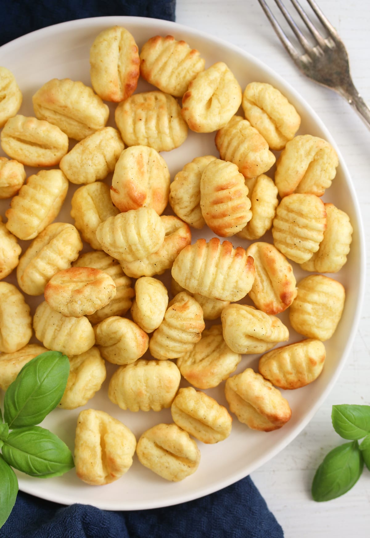 close up plate full of golden brown gnocchi with fresh basil.