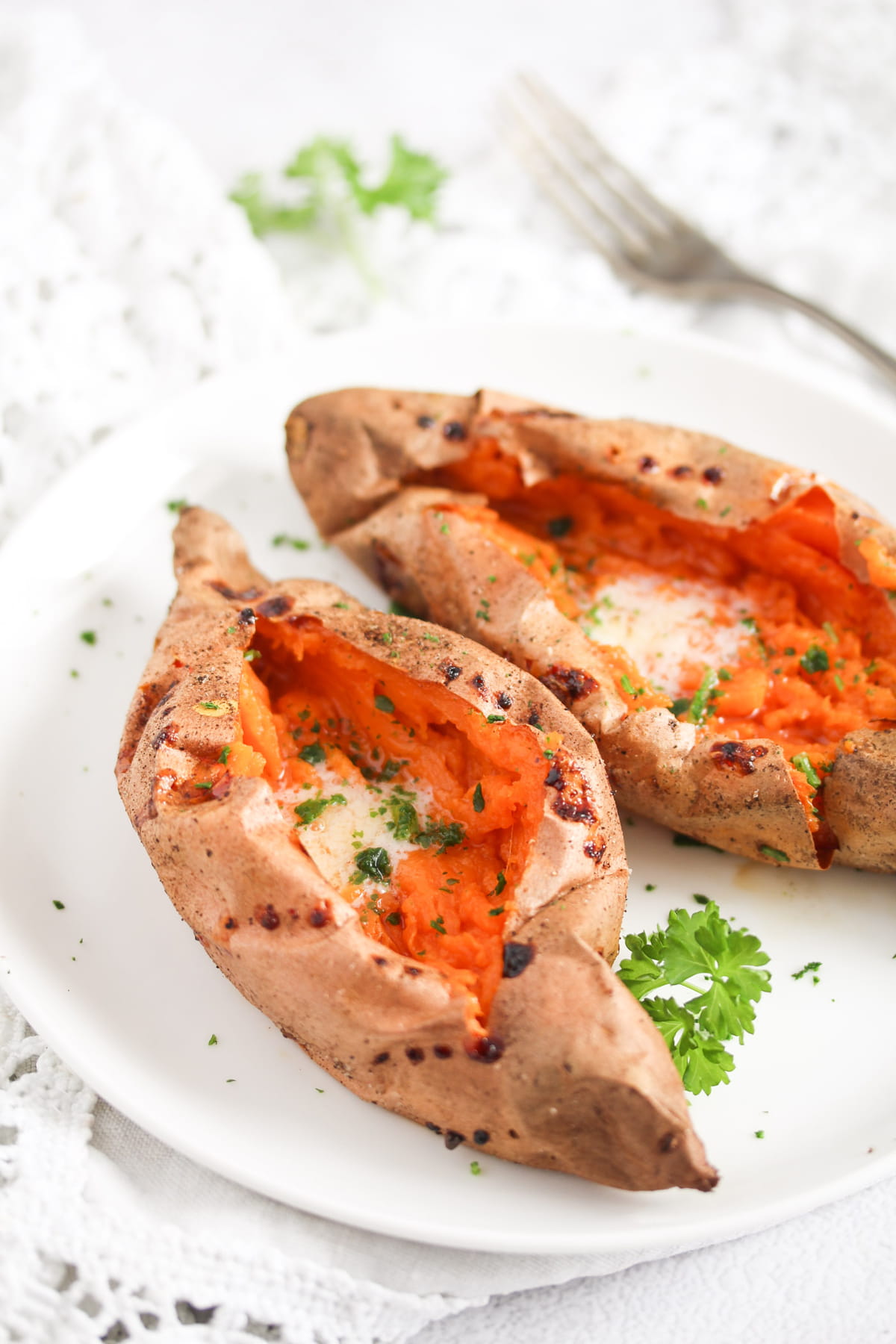 two baked sweet potatoes on a white plate sprinkled with parsley.