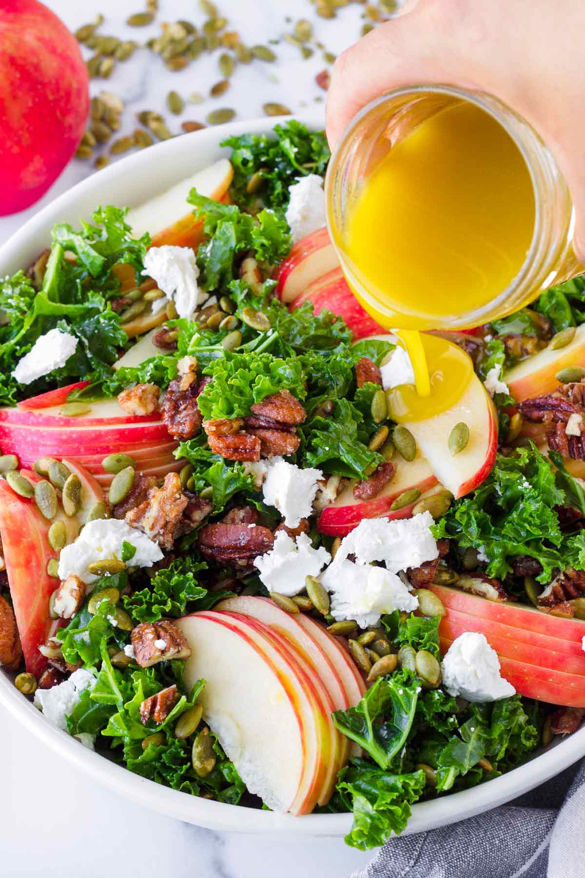 pouring dressing over kale and apple salad.