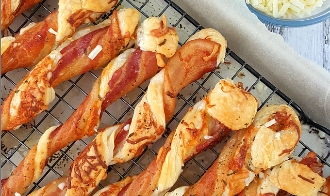 puff pastry twist with bacon and cheese arranged on a rack with a bowl of cheese near by.