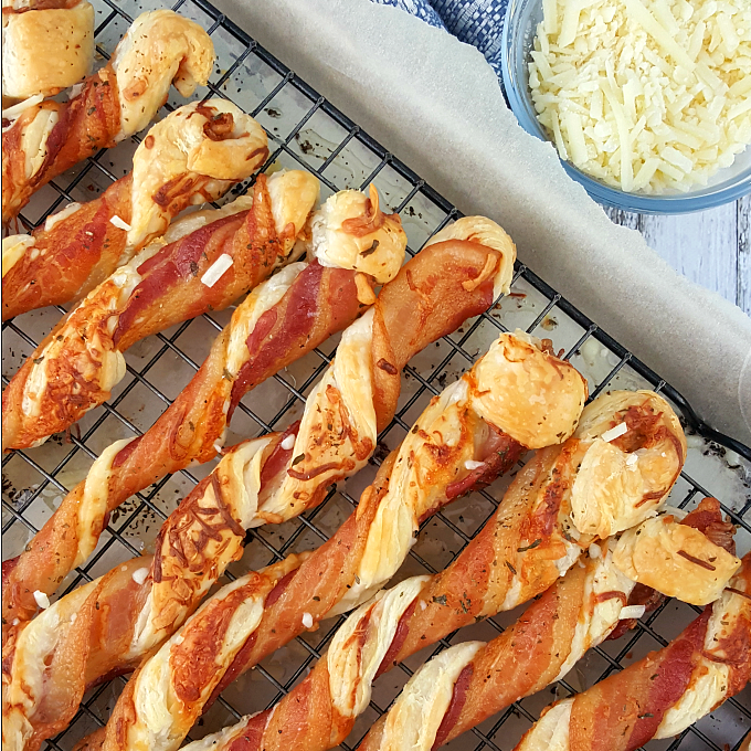 puff pastry twist with bacon and cheese arranged on a rack with a bowl of cheese near by.