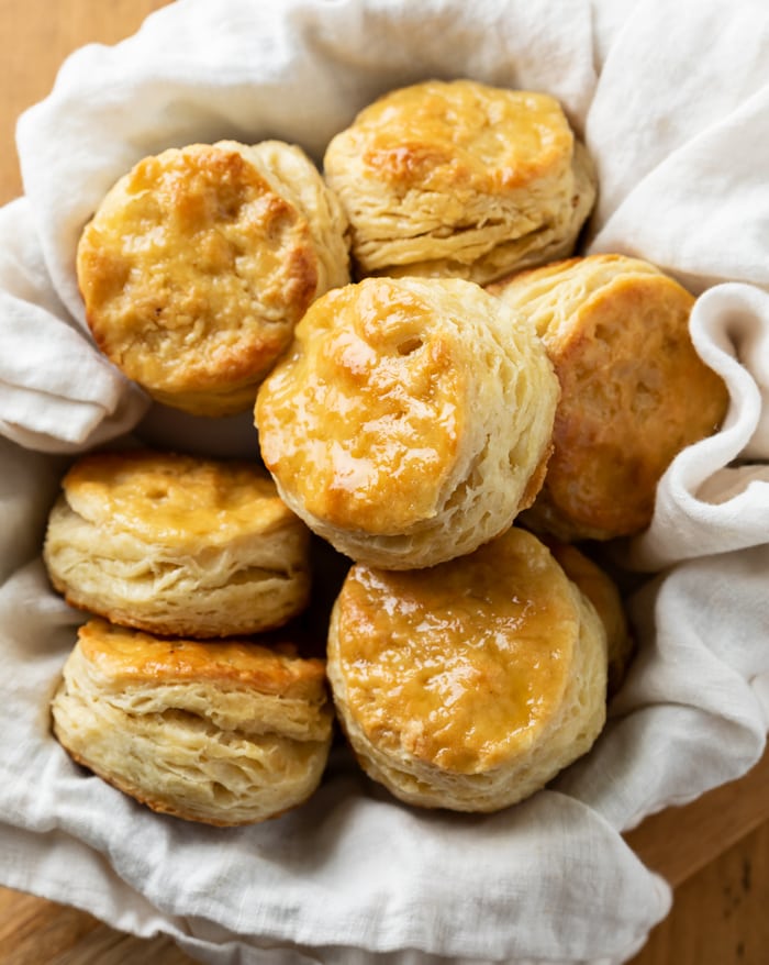 many buttermilk biscuits in a basket on a white cloth.