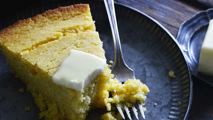 slice of cornbread with butter on top eaten with a fork from a blue plate.