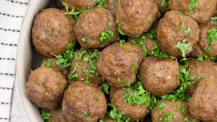 overhead view of many oven-baked meatballs sprinkled with parsley.