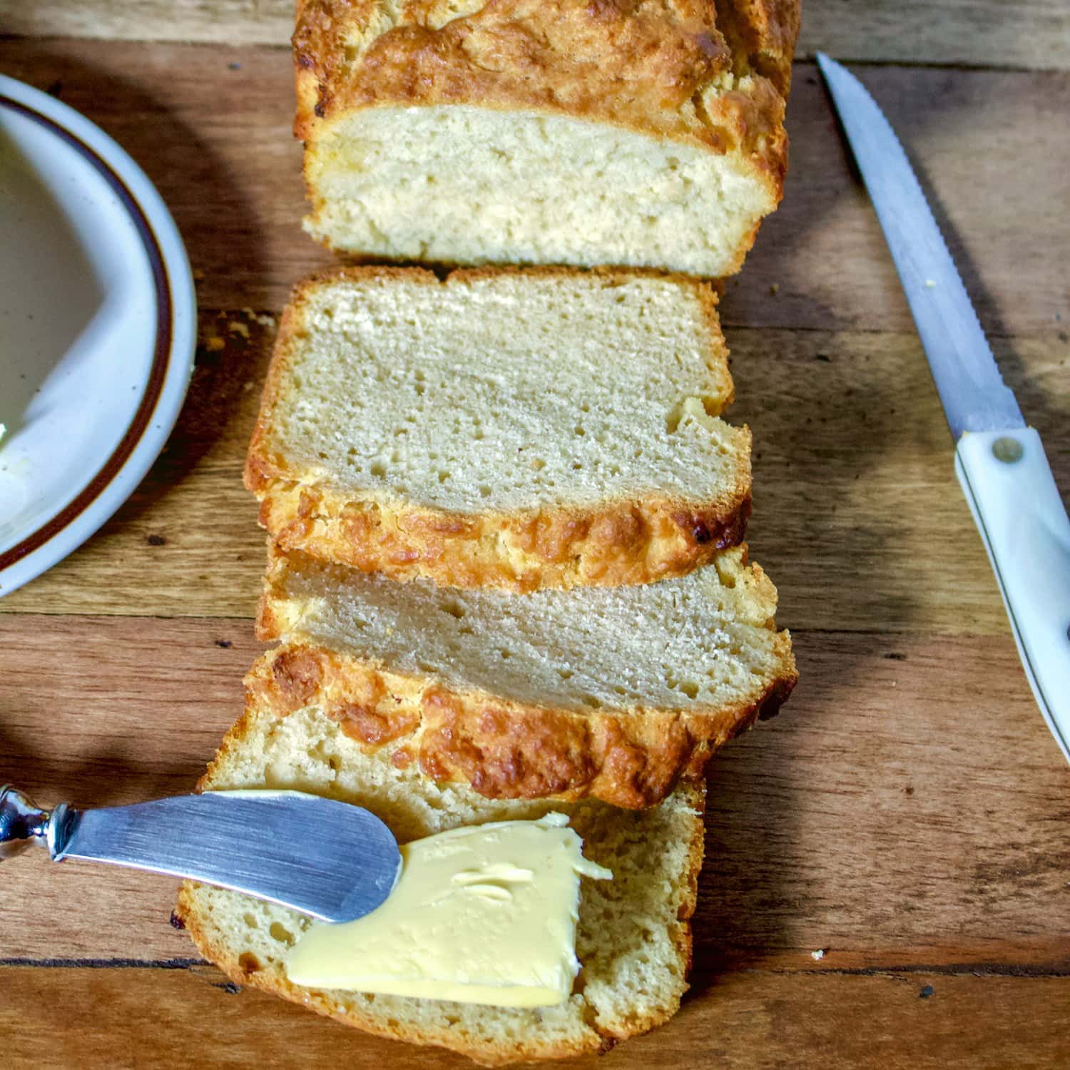 sliced beer bread on a rustic table with a knife beside it.