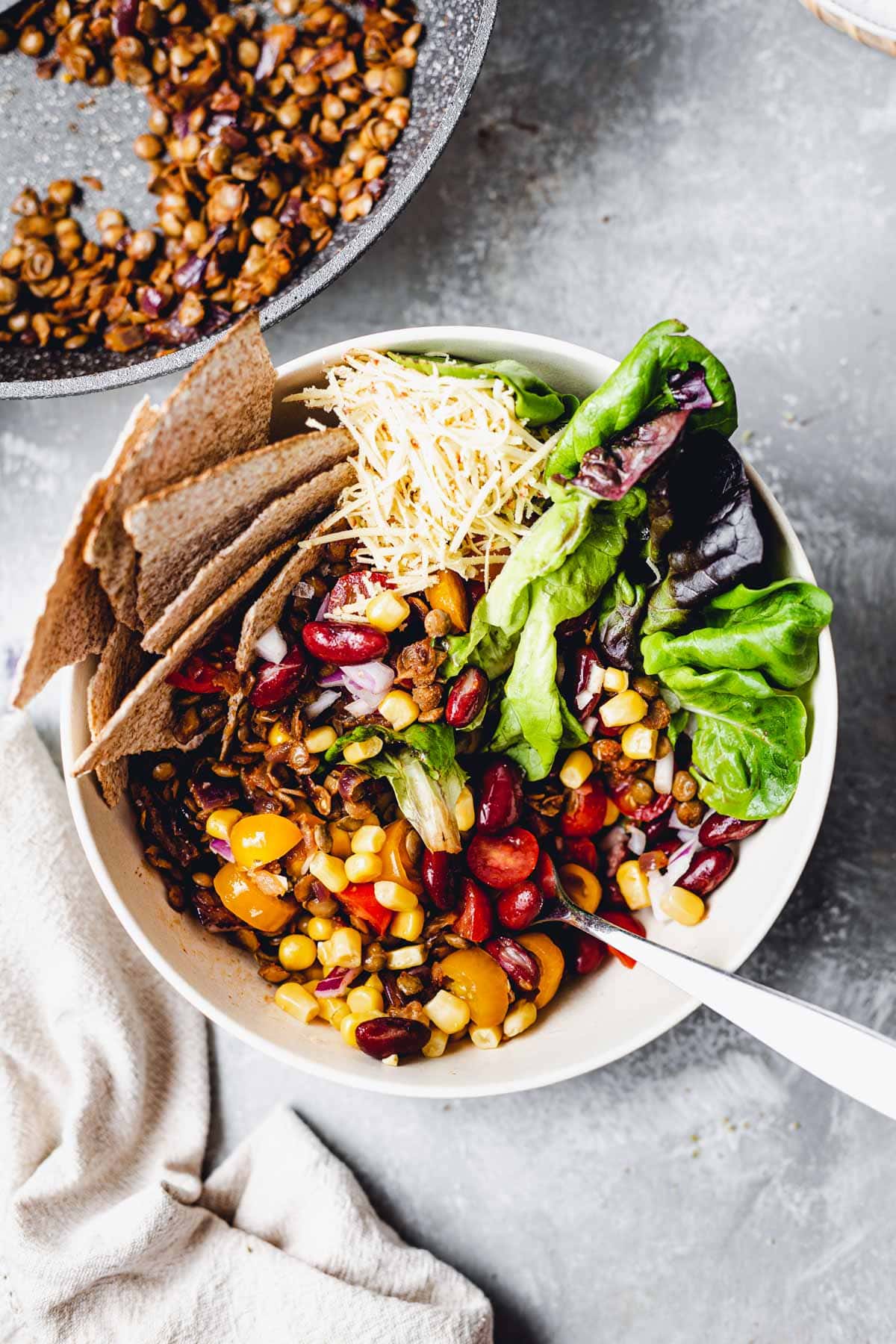 bowl with vegan taco salad with corn, avocado, tortillas, tomatoes.