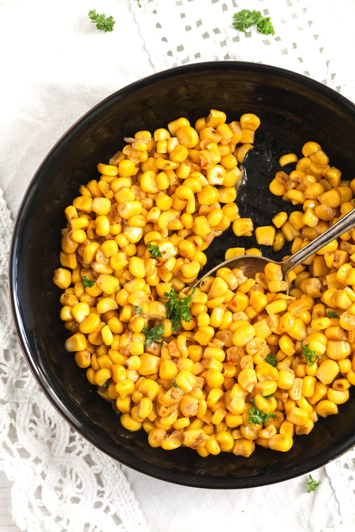 bowl of cooked corn kernels wit a spoon in it.