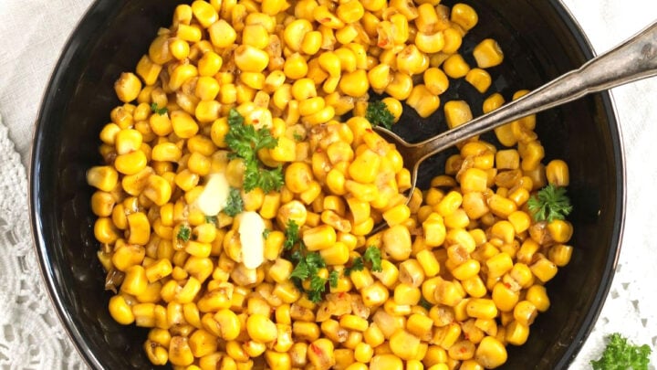 cooked corn from a can in a black bowl with butter on top.