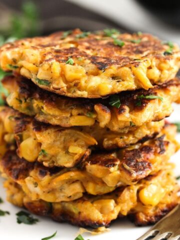 five corn and zucchini fritters stapled on a plate.