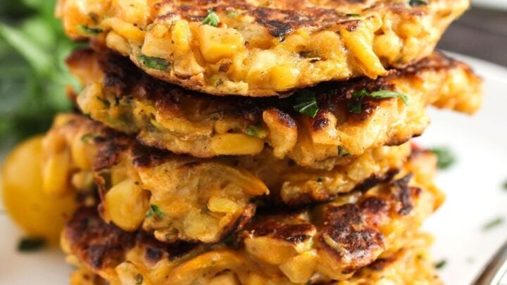 five corn and zucchini fritters stapled on a plate.